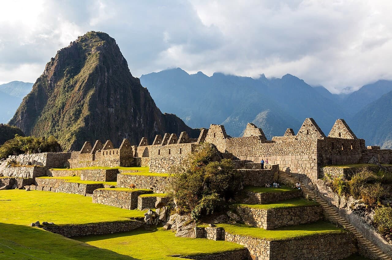 Stone houses and green agricultural terraces at Machu Picchu, with Huayna Picchu rising behind the citadel.
