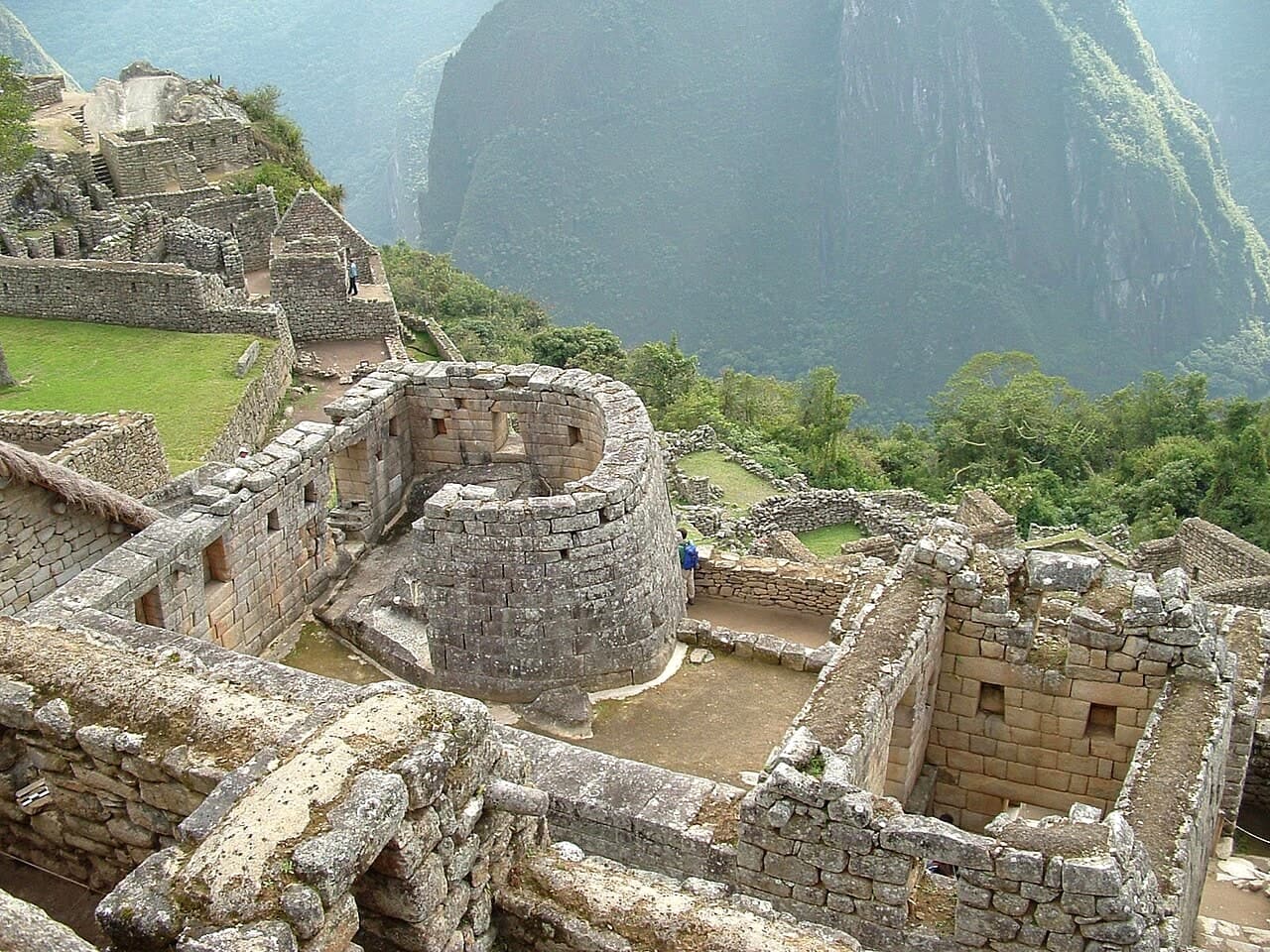 The curved stone wall of the Temple of the Sun at Machu Picchu, with Huayna Picchu in the distance.