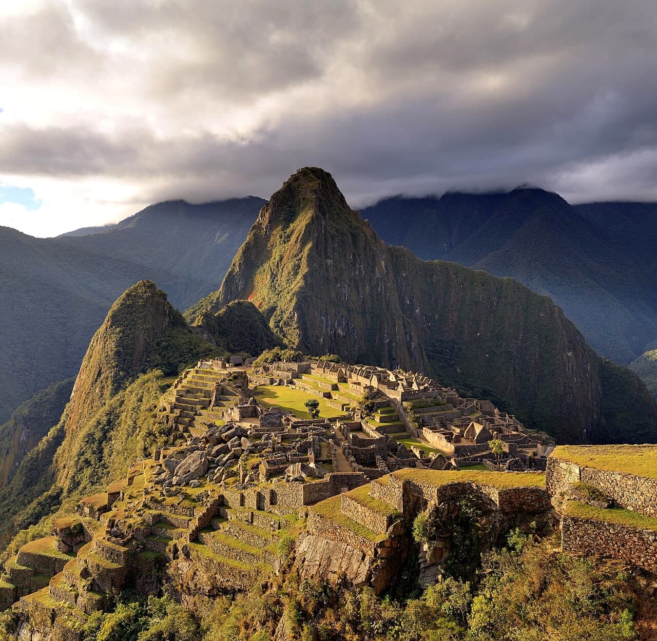 Machu Picchu on its ridge at twilight, with Huayna Picchu under cloud and the Urubamba valley below.